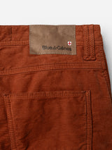 Close-up of BGpaulo Ottawa V3 Trousers in Ginger Bread Orange, a slim fit chino pant by Blue de Gênes. Crafted from rust-colored dobby corduroy, these trousers feature a brown leather patch above the back pocket embossed with the Blue de Gênes name and adorned with a small red and white shield emblem. Classic texture meets modern tailoring for a refined look.