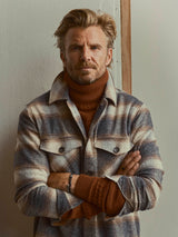 A man with arms crossed wearing a burnt-orange, textured BGstu Rollneck Knit - Ginger Bread Orange under a plaid button-down shirt.