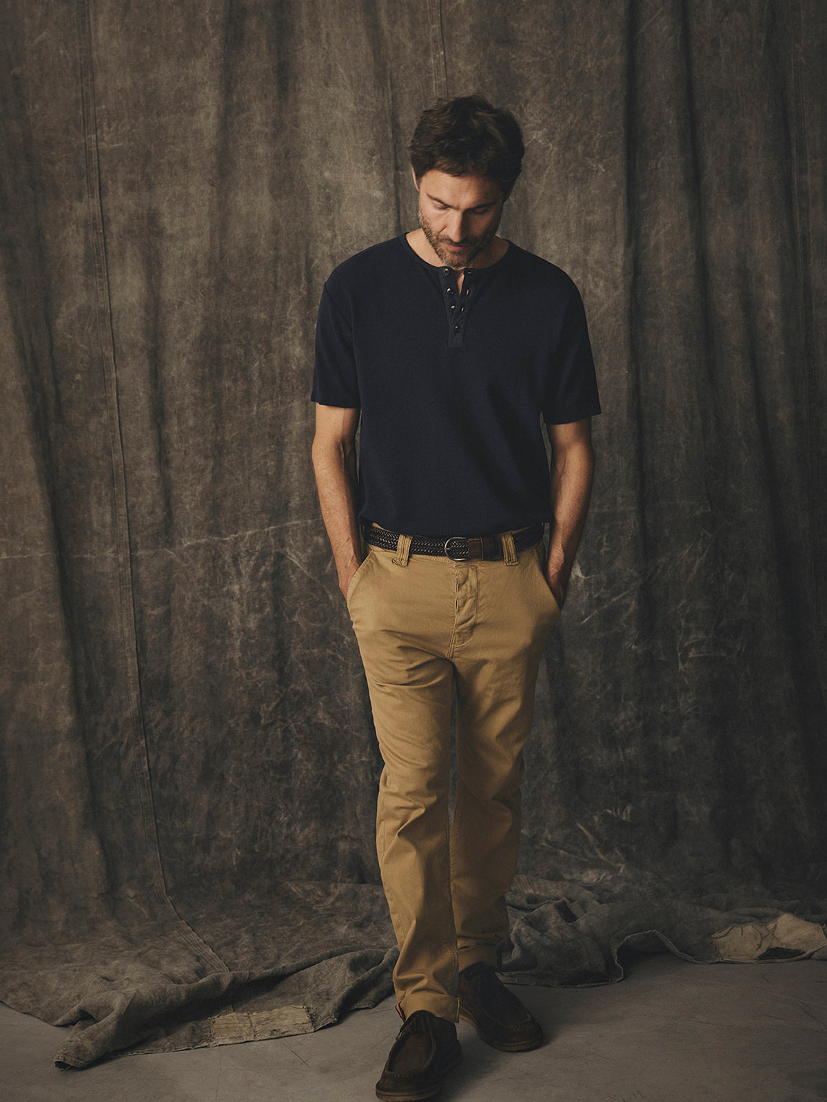 A man wearing a navy henley shirt and enzyme-washed BGpaulo Pavia V3 Chino - Khaki pants with his hands in his pockets.