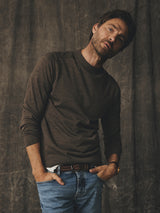 A man posing with his hands in his pockets, wearing a Blue de Gênes BGhamish Crewneck Knit - Sepia Tint Brown, blue jeans, and a woven belt.