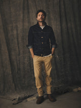 A man wears a dark denim jacket over a white shirt and Blue de Gênes BGmenzo Vecchio Chino - Pale Khaki pants with brown boots.