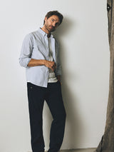A man wears a white t-shirt, an unbuttoned blue and white striped shirt, and vintage-look Blue de Gênes BGmenzo Vecchio Chino - Dark Navy trousers.