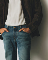 A person wearing BGvinci Girisha Used Jeans in comfortable stretch denim with their hands in the front pockets, paired with a white t-shirt and a dark brown jacket.