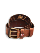 The Cintura Belt - Cognac by Blue de Gênes is a rolled brown leather belt with a brass buckle and a small red and white shield emblem on the loop, shown on a white background. Inside, gold text and a crest add vintage military appeal.