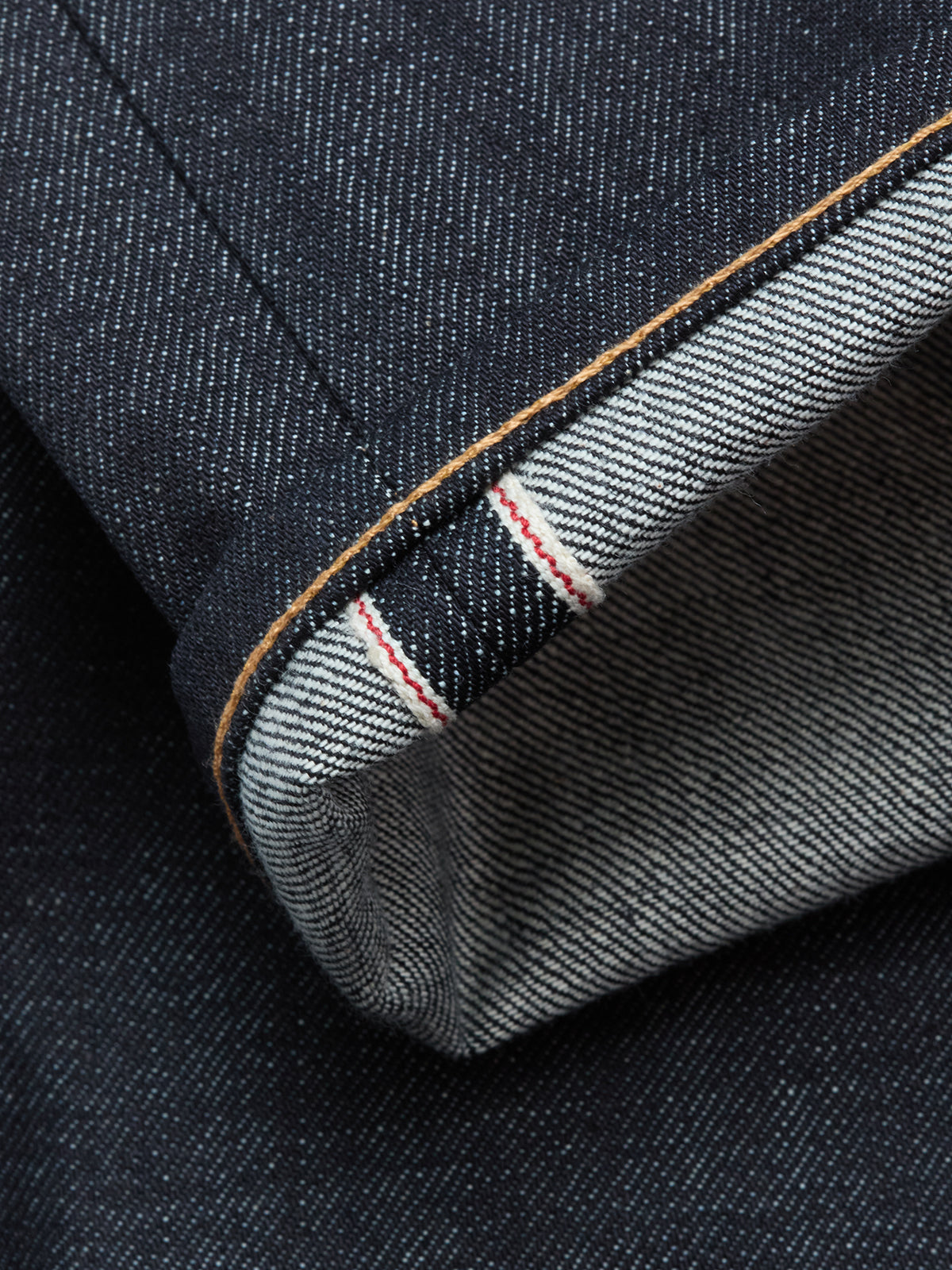 Close-up of the Blue de Gênes Giacomo Selvedge V2 Jeans in raw dark blue denim, featuring a cuffed hem that highlights the white inner selvedge seam with a distinctive red line and showcases the textured weave.