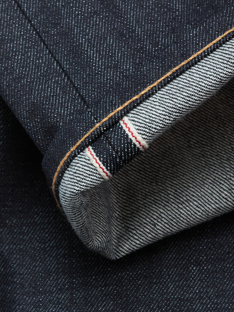 Close-up of the Blue de Gênes Giacomo Selvedge V2 Jeans in raw dark blue denim, featuring a cuffed hem that highlights the white inner selvedge seam with a distinctive red line and showcases the textured weave.