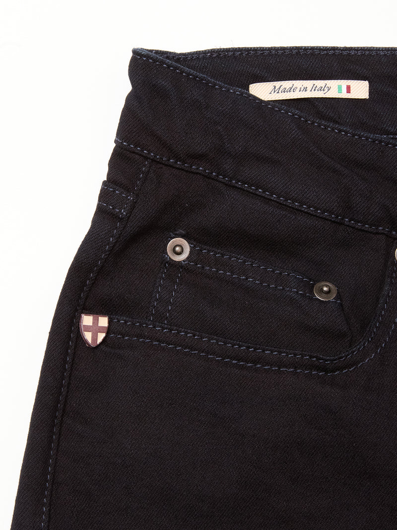 Close-up of the upper section of Blue de Gênes Vinci Venom Blk Jeans - Dark Denim, showing a small front pocket, metal rivet, pink and white cross emblem, and a Made in Italy label with flag. Crafted from comfort stretch twill for ease.
