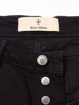 Close-up of Vinci Venom Blk Jeans - Dark Denim by Blue de Gênes, featuring black comfort stretch twill, three exposed silver shield-engraved buttons with the brand name, and a cream label with the brand logo stitched inside the waistband.