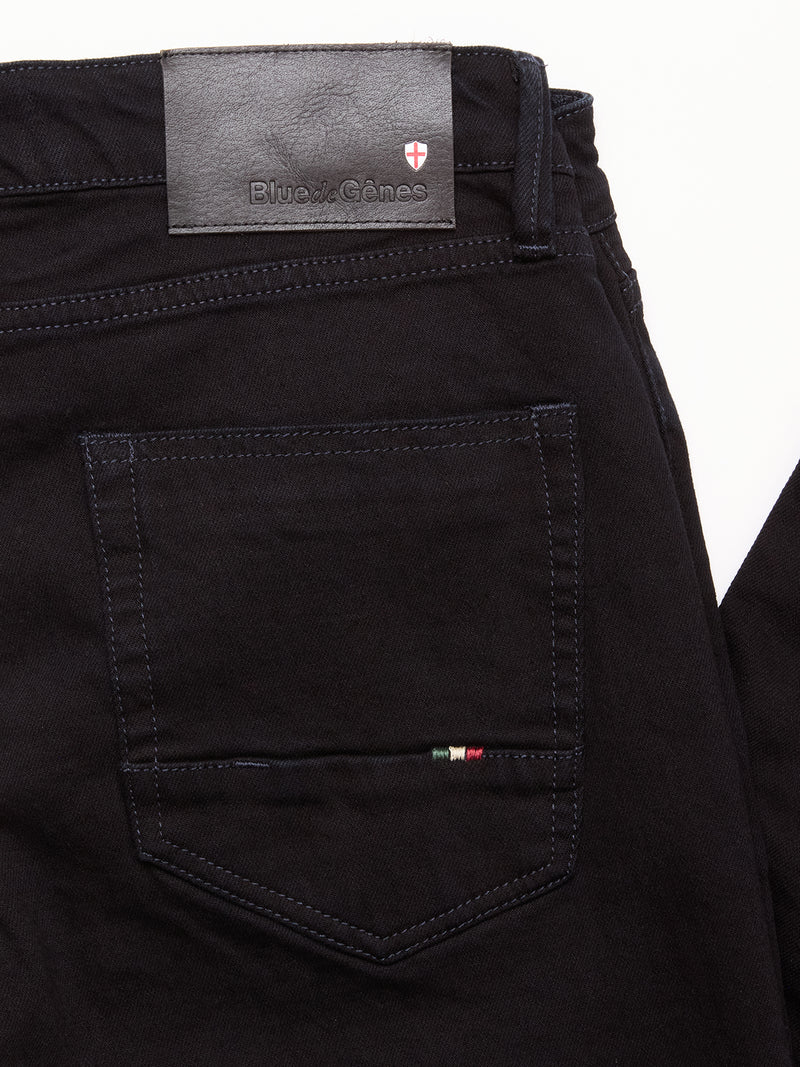 Close-up of the back pocket on Blue de Gênes Vinci Venom Blk Jeans - Dark Denim, with a black leather brand patch, dark stitching, a striped tag, and small red and white logo above. Made from black comfort stretch twill.