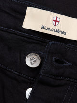 Close-up of Vinci Venom Blk Jeans in dark denim by Blue de Gênes, featuring a metal button and waistband label with the brand’s name and red cross emblem on a white background, made from comfort stretch twill.