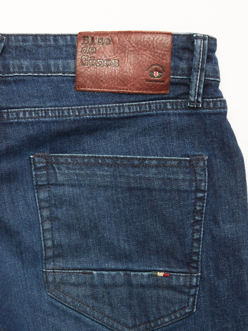 Close-up of the back pocket of Vinci Used Jeans - Used by Blue de Gênes, showing a brown leather patch embossed with the brand and eye symbol. Made in Italy from comfort stretch blue denim, regular fit.