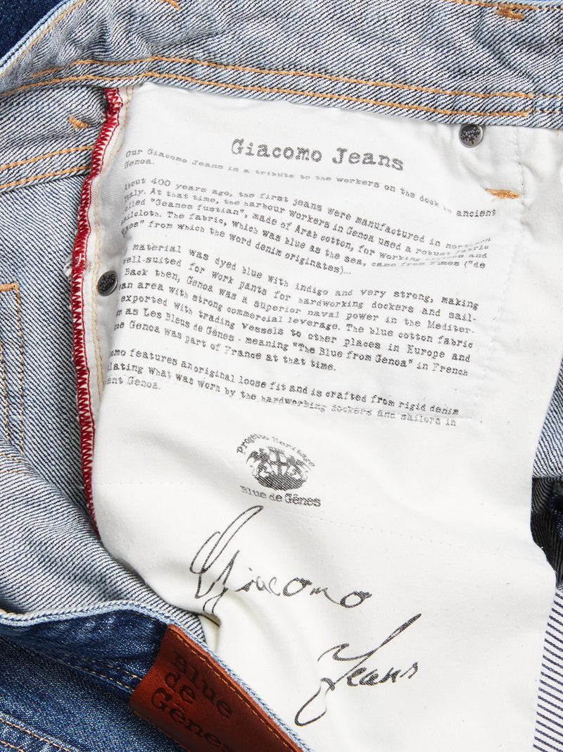 Close-up of the inside pocket of Giacomo Osaka Jeans - Dark Denim by Blue de Gênes, showing a white label with brand history details and a brown leather patch with the brand name on the waistband.