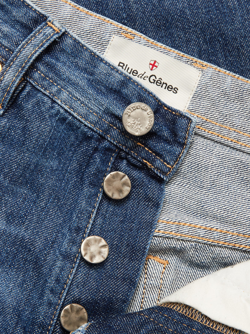 Close-up of Giacomo Osaka Jeans - Dark Denim by Blue de Gênes, featuring undone metallic buttons and the brand label on the inner waistband. The rigid denim displays visible orange stitching and textured fabric detail.