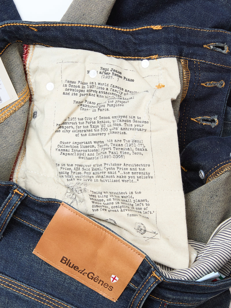 Close-up of the inside of Repi Dark Vintage Jeans - Mid Blue Denim by Blue de Gênes, showing a sewn-in fabric label with printed details and a tan leather patch on the waistband featuring Blue de Gênes and a small red and white flag.