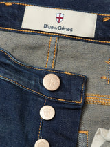 Close-up of Blue de Gênes Repi Dark Vintage Jeans in mid-blue denim, featuring a regular slim fit, visible buttons and stitching, comfort stretch fabric, and a red cross emblem on the label above the waistband.