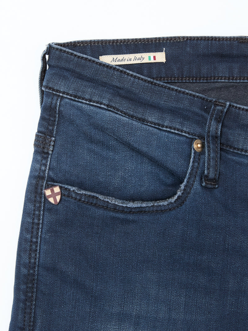 A close-up of Blue de Gênes Repi BlueBlk Used Jeans in blue-black denim shows the front pocket, metal rivet, a badge, and a Made in Italy label with flag, highlighting the comfort stretch fabric for ease and style.