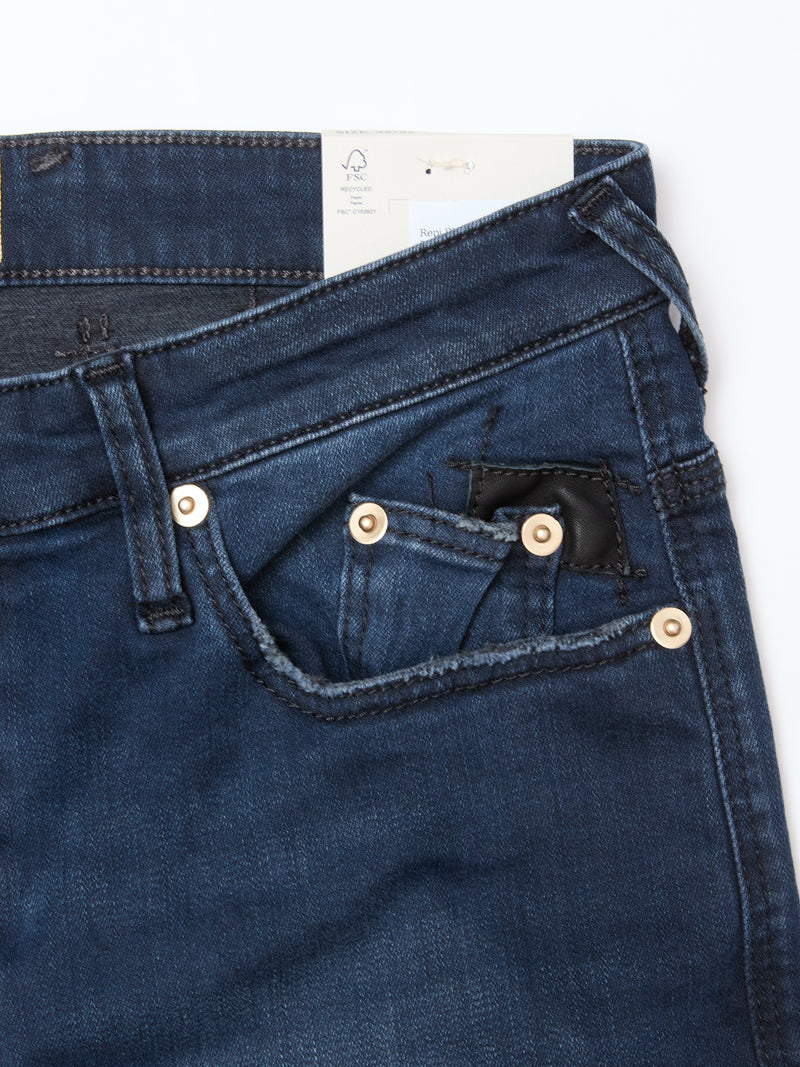 Close-up of the waist and front pockets of Blue de Gênes Repi BlueBlk Used Jeans in blue-black denim, featuring gold rivets. A clothing tag is partially visible inside the waistband against a white background.
