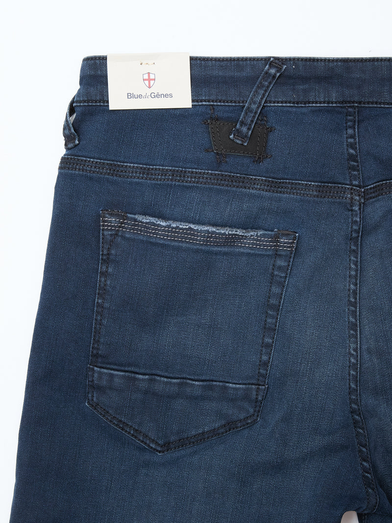 Close-up of the back of Blue de Gênes Repi BlueBlk Used Jeans in blue-black stretch denim, showing a leather patch by the waistband and visible back pocket. Blue de Gênes label appears at the top.