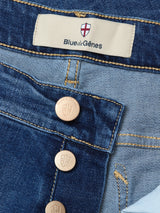 Close-up of Blue de Gênes Recco Blue Vintage Jeans in vintage wash, highlighting comfort denim, visible brass buttons, red and white shield logo label, detailed stitching, rich denim texture, and tapered legs.
