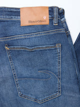 Close-up of the Recco Blue Vintage Jeans in vintage wash by Blue de Gênes, showing a tan leather brand patch, red shield logo above the right pocket, and contrast stitching—crafted from comfort denim for a relaxed fit.