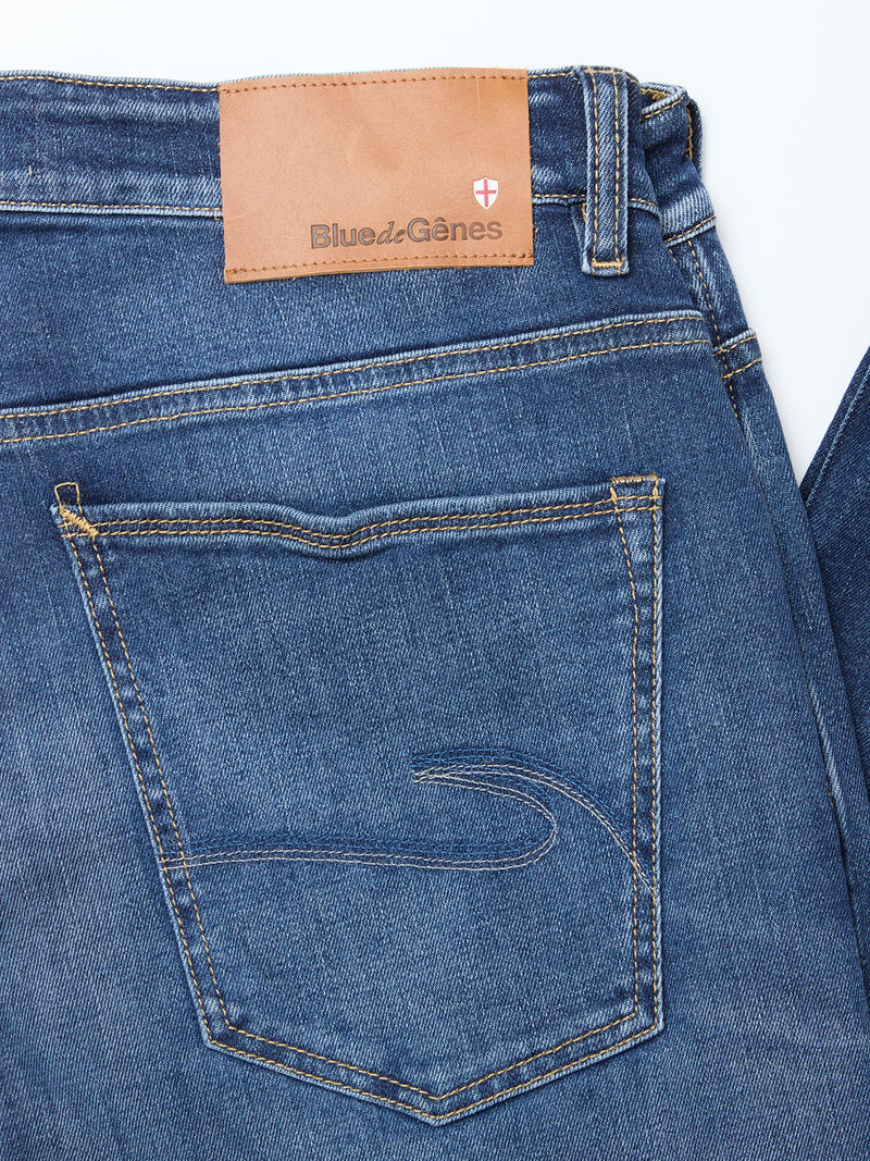 Close-up of the Recco Blue Vintage Jeans in vintage wash by Blue de Gênes, showing a tan leather brand patch, red shield logo above the right pocket, and contrast stitching—crafted from comfort denim for a relaxed fit.
