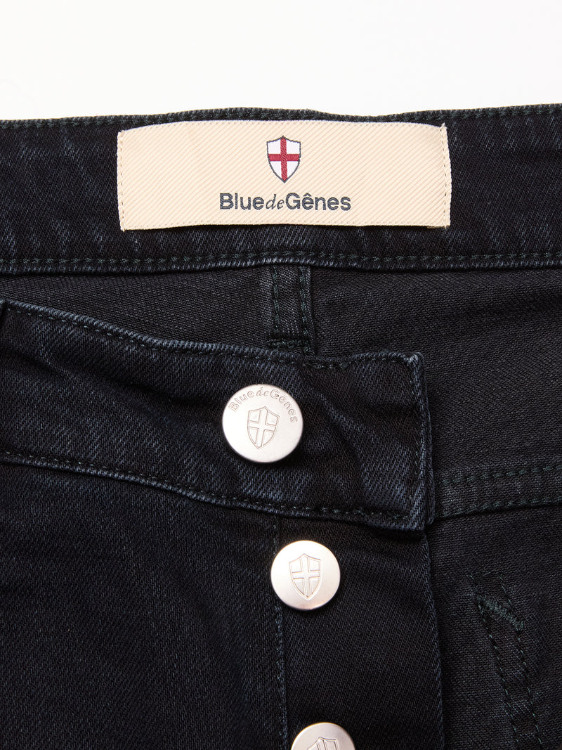 Close-up of the waistband on Blue de Gênes Recco BlueBlk Jeans in blue-black denim, showcasing silver shield-logo buttons and a fabric label reading Blue de Gênes with a red and white shield emblem—ideal relaxed regular fit jeans.