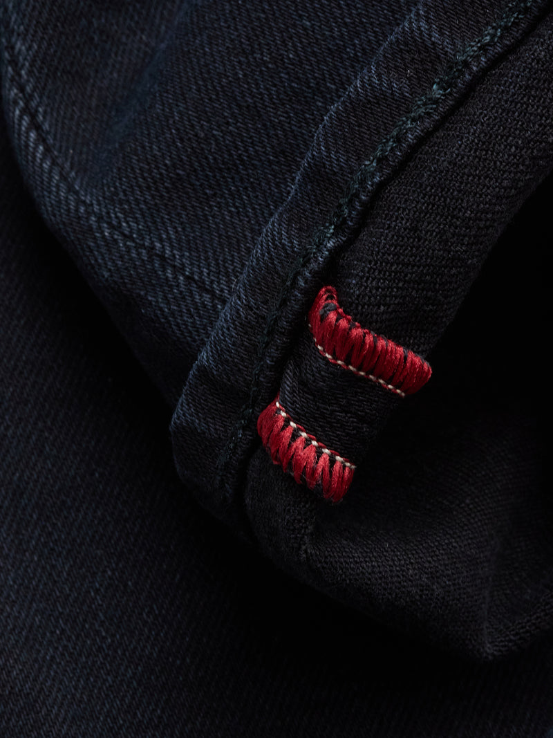 Close-up of Blue de Gênes Recco BlueBlk Jeans in blue-black Italian denim, showcasing a folded hem with signature red and white stitching—an iconic detail on these classic tapered leg jeans.