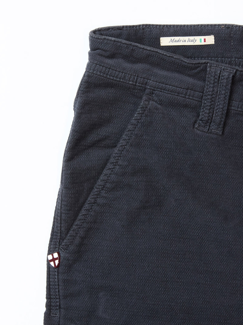 Close-up of Blue de Gênes BGpaulo Ottawa Trousers in dark navy dobby corduroy, showing the front pocket, belt loop, an embroidered shield emblem by the pocket, and a small "Made in Italy" label near the waistband.