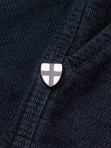 A close-up of dark denim with a shield-shaped enamel pin, white with a red cross—perfectly paired with Blue de Gênes BGpaulo Ottawa Trousers in Dark Navy for a refined, distinctive touch.