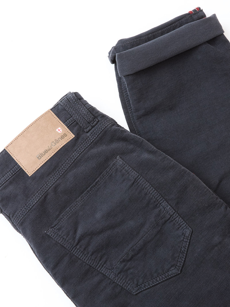 A pair of folded BGpaulo Ottawa Trousers in dark navy by Blue de Gênes, featuring a brown leather waistband patch and visible back pocket, made in Italy, displayed on a white background.
