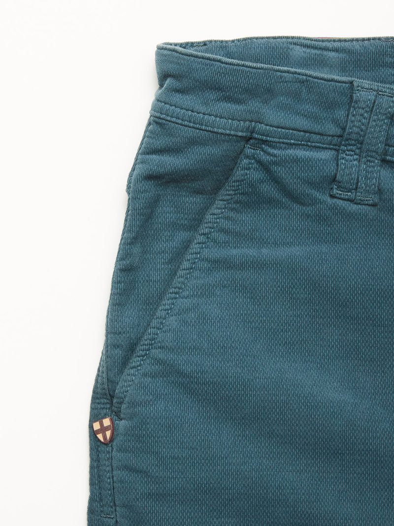 Close-up of the upper section of Blue de Gênes BGpaulo Ottawa Trousers in Dark Slate, featuring a belt loop, front pocket, and a small round emblem with a red cross on beige near the pocket seam.