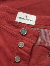Close-up of BGpaulo Ottawa Trousers - Henna by Blue de Gênes in red dobby corduroy, with metal buttons partially undone to reveal a white Blue de Gênes label with a red cross and an interior lined in striped fabric.