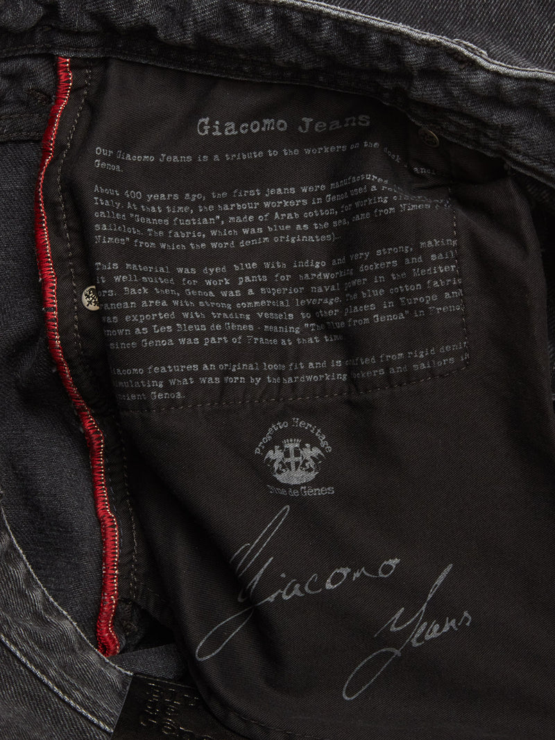 Close-up of the inside label on Blue de Gênes Giacomo BLK Used Jeans - Grey Denim, showing white heritage text, visible stitching, and red trim—crafted from rigid denim and made in Italy.