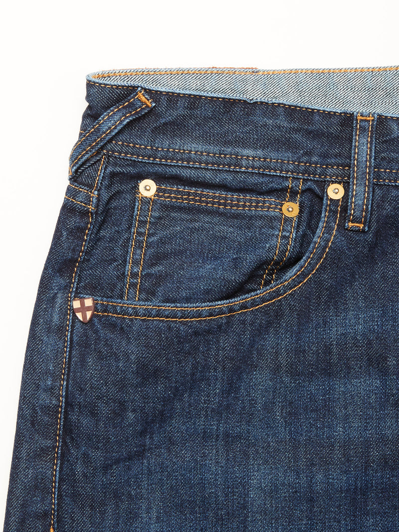 Close-up of the front pocket on Blue de Gênes Giacomo Dark Horse Jeans in denim blue, highlighting golden stitching, metal rivets, and a red cross shield patch—signature details of these relaxed loose fit jeans made in Italy.