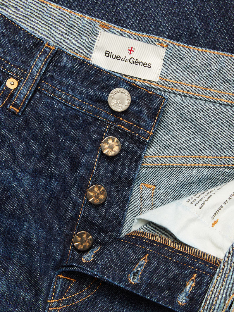 Close-up of Blue de Gênes Giacomo Dark Horse Jeans in denim blue, showcasing rigid fabric, button fly, orange stitching, a white Blue de Gênes label inside the waistband, and a relaxed loose fit style.