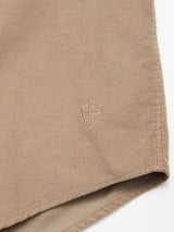 Close-up of the Blue de Gênes Zamboni Velu Shirt - Fungi, a garment-dyed baby corduroy piece with a small embroidered shield and cross near the hem, shown against a plain white background.