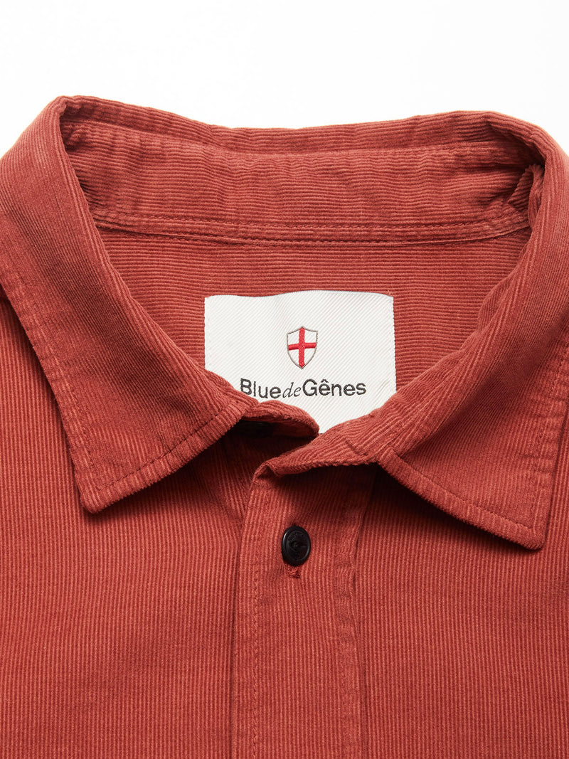 A close-up of the Zamboni Velu Shirt - Henna by Blue de Gênes, featuring a rust-colored baby corduroy collar with a single black button and a visible label with a small red shield emblem.