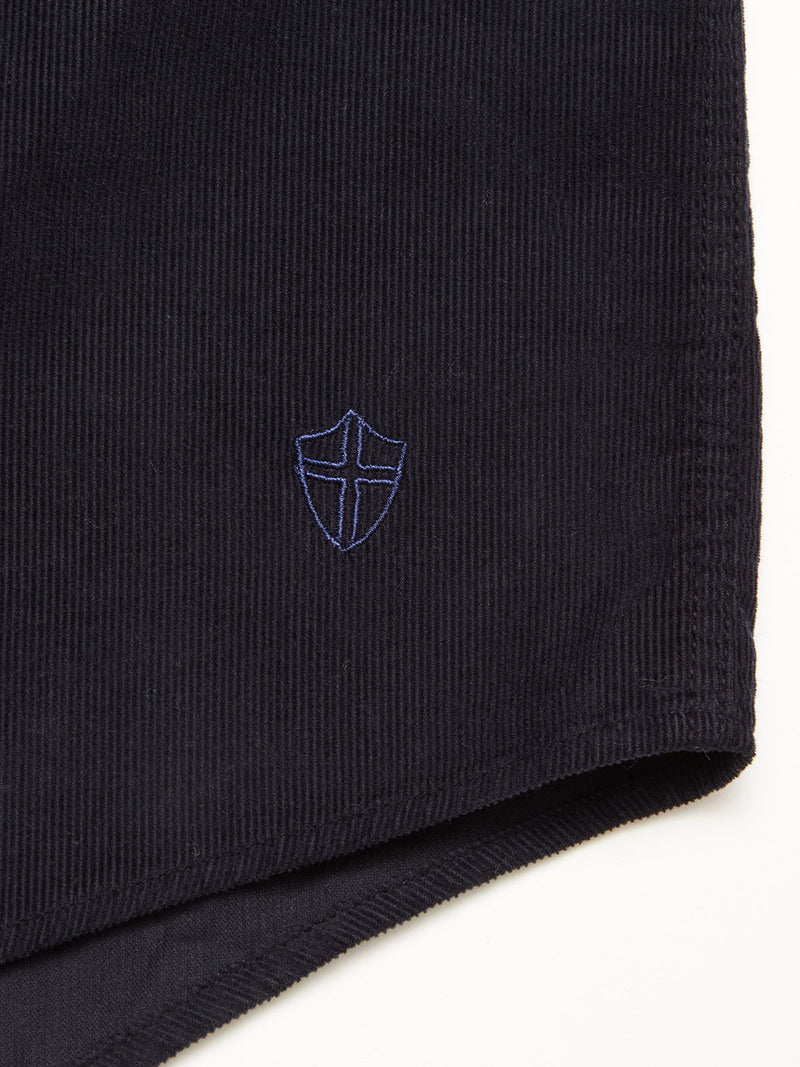 Close-up of the Zamboni Velu Shirt by Blue de Gênes in navy baby corduroy, garment dyed for depth, featuring a small blue embroidered shield with a cross near the hem—a signature brand detail.