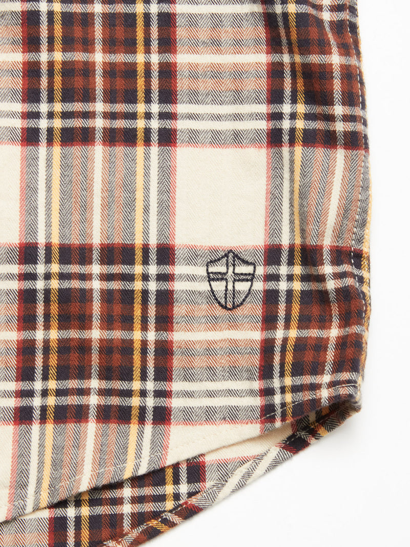 A close-up of the Robertino Brush Shirt - Stone by Blue de Gênes, showcasing plaid fabric in red, yellow, navy, and white with an embroidered black shield-like emblem and crafted from Sidogras cotton.