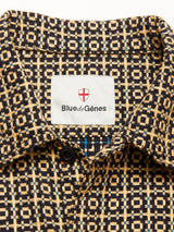 Close-up of the collar on the Manga Overshirt - Black Pattern by Blue de Gênes, featuring a beige and black geometric design, a red shield logo above the brand label, and a visible black button below.
