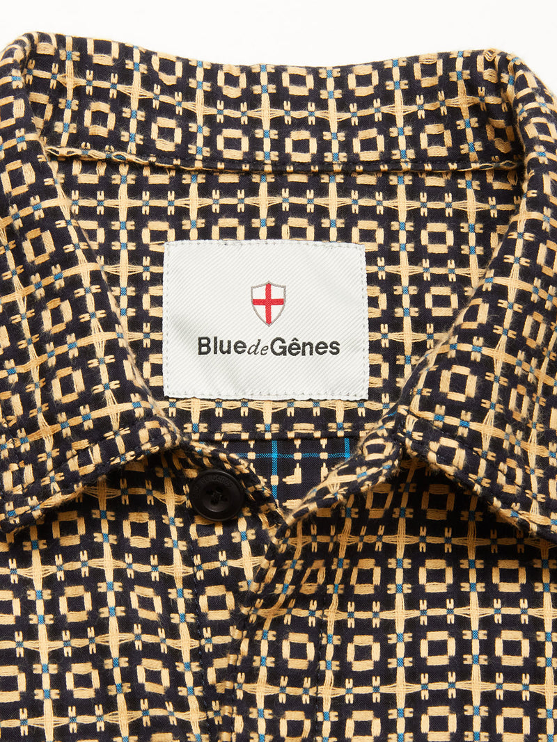 Close-up of the collar on the Manga Overshirt - Black Pattern by Blue de Gênes, featuring a beige and black geometric design, a red shield logo above the brand label, and a visible black button below.