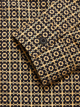 Close-up of the Blue de Gênes Manga Overshirt - Black Pattern, showing its textured cotton fabric and sleeve with a black button, featuring a geometric design in tan, black, and blue squares and lines.