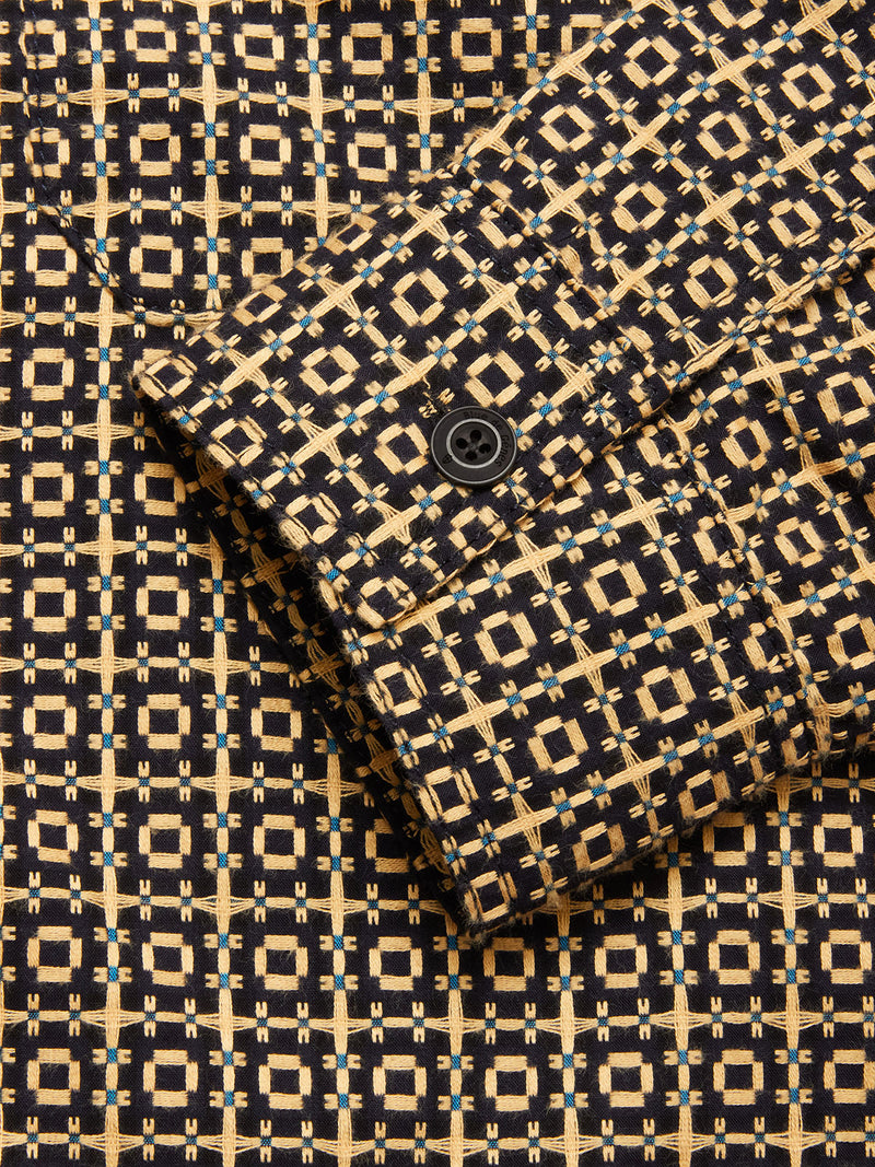 Close-up of the Blue de Gênes Manga Overshirt - Black Pattern, showing its textured cotton fabric and sleeve with a black button, featuring a geometric design in tan, black, and blue squares and lines.