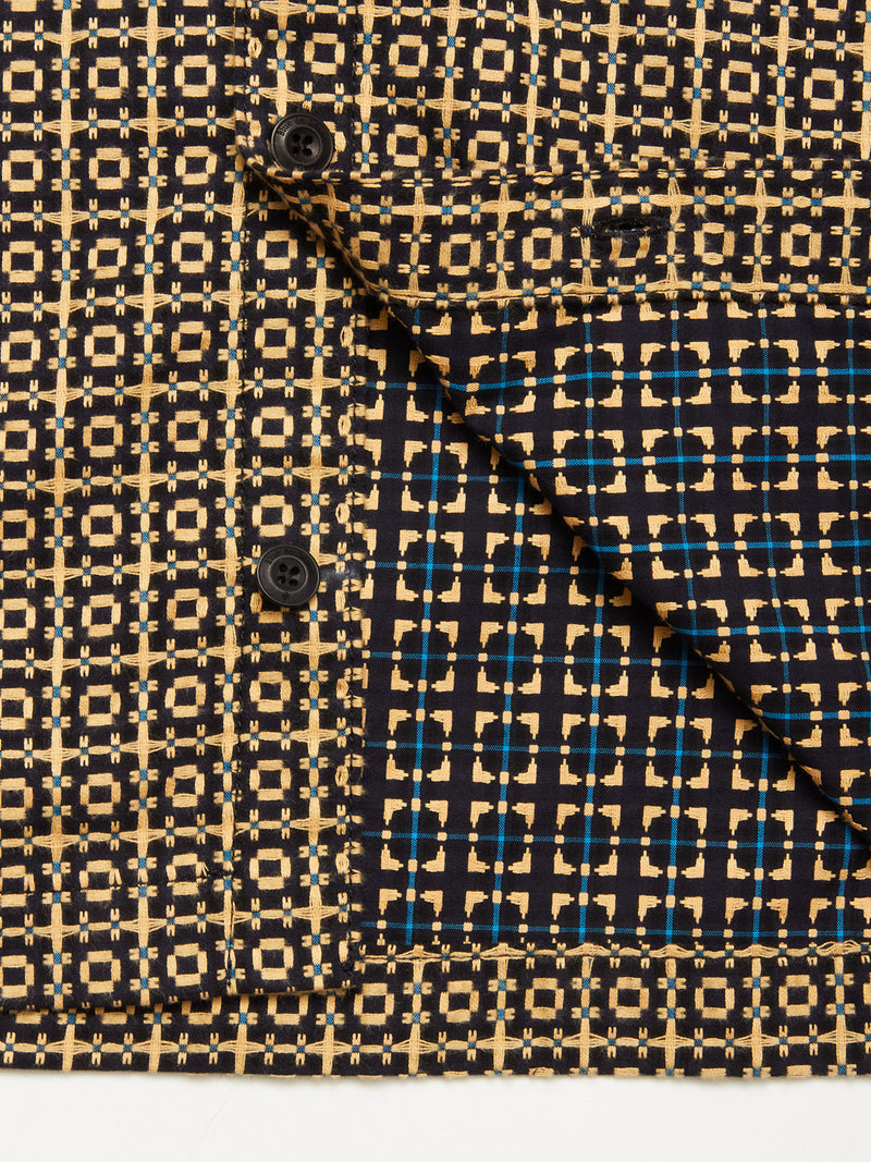 Close-up of the Blue de Gênes Manga Overshirt - Black Pattern. The cotton overshirt displays a yellow, blue, and black grid design with two black buttons and a folded flap revealing the reverse side and its modern workwear style.