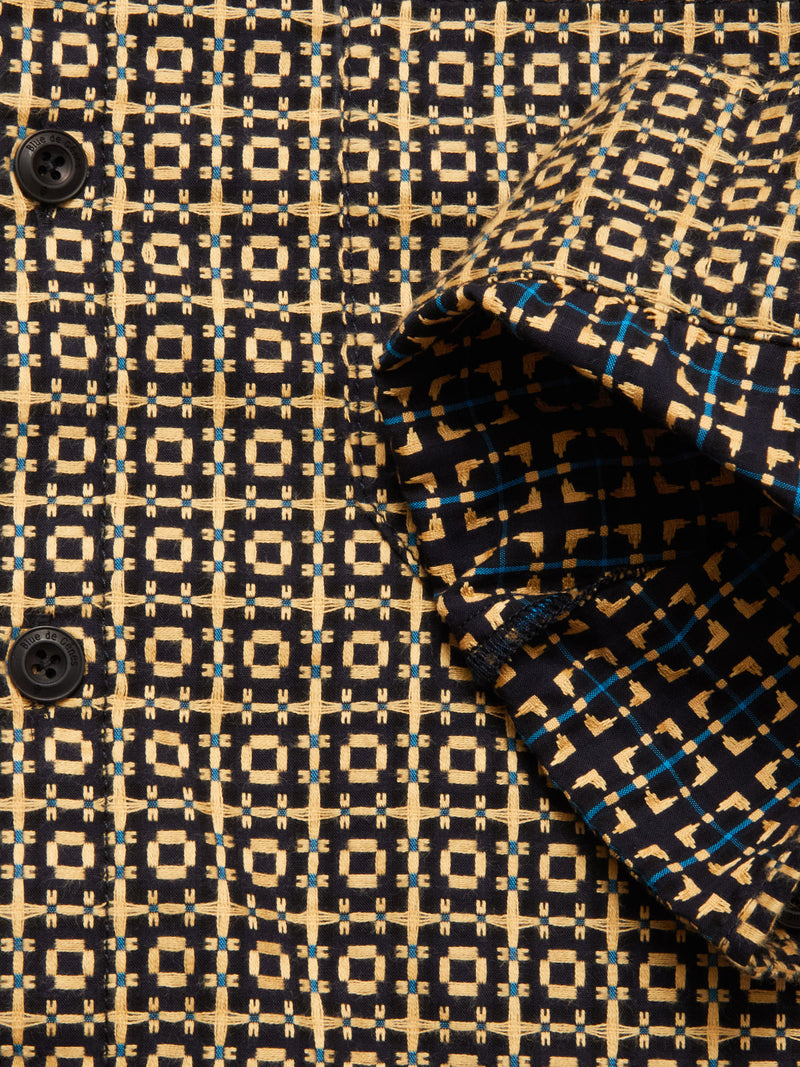 Close-up of the Blue de Gênes Manga Overshirt in a black pattern, showing black buttons and a geometric design with beige, blue, and black squares. The folded cuff highlights the distinctive grid motif.