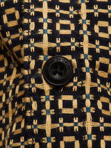 Close-up of a black “rue de Côtes” button on the Blue de Gênes Manga Overshirt—black cotton with yellow geometric patterns and small blue accents.