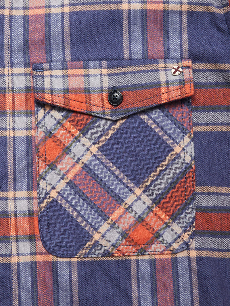 Close-up of the Blue de Gênes Yodo Check Overshirt - Multi Check pocket. Soft-touch moleskin fabric with intersecting blue, orange, white, and beige lines; a red embroidered X decorates the flap's top right corner.