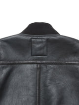 Close-up of the upper back of the Rufo Shearling Jacket - Scarab by Blue de Gênes, featuring black natural sheepskin, visible stitching, textured leather, a ribbed black collar, and a rectangular stitched patch.