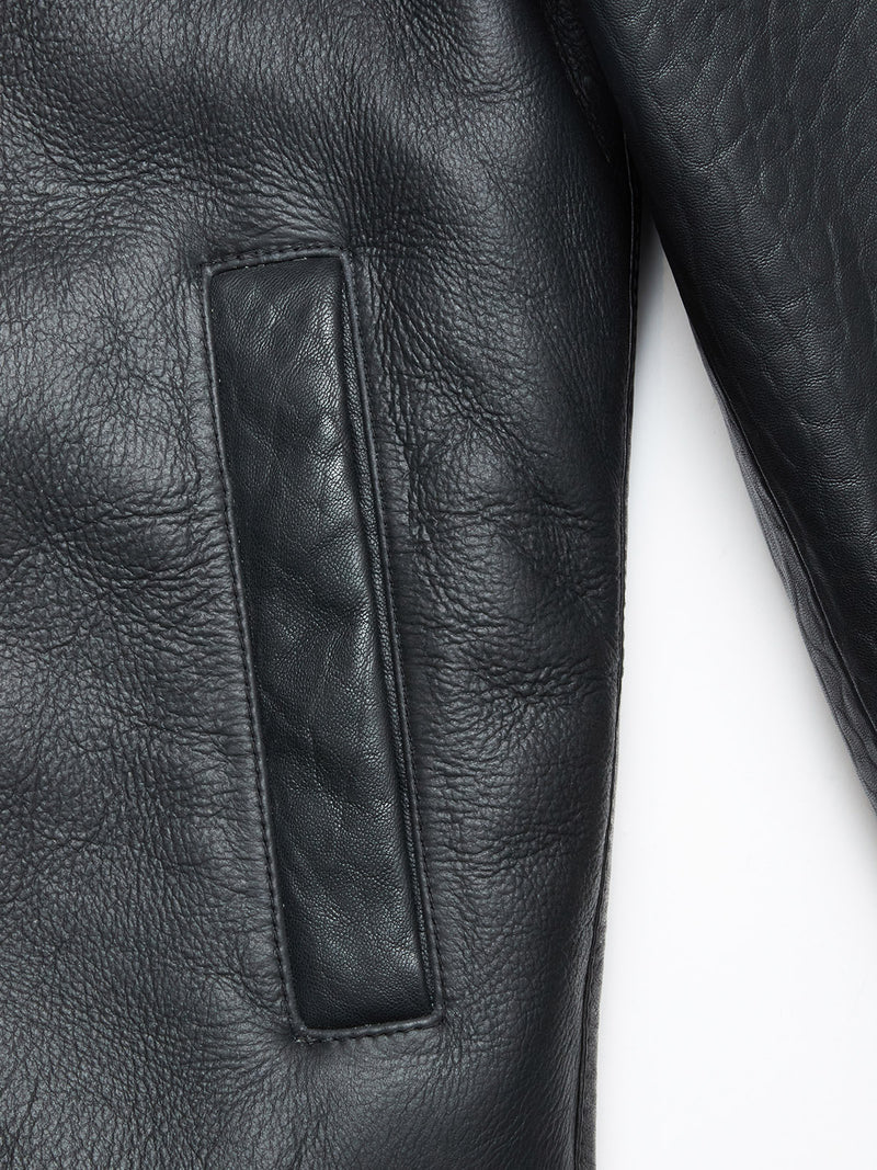 Close-up of the Rufo Shearling Jacket - Scarab by Blue de Gênes, highlighting its black textured shearling, rectangular side pocket with visible stitching, and a partially visible sleeve on the right.
