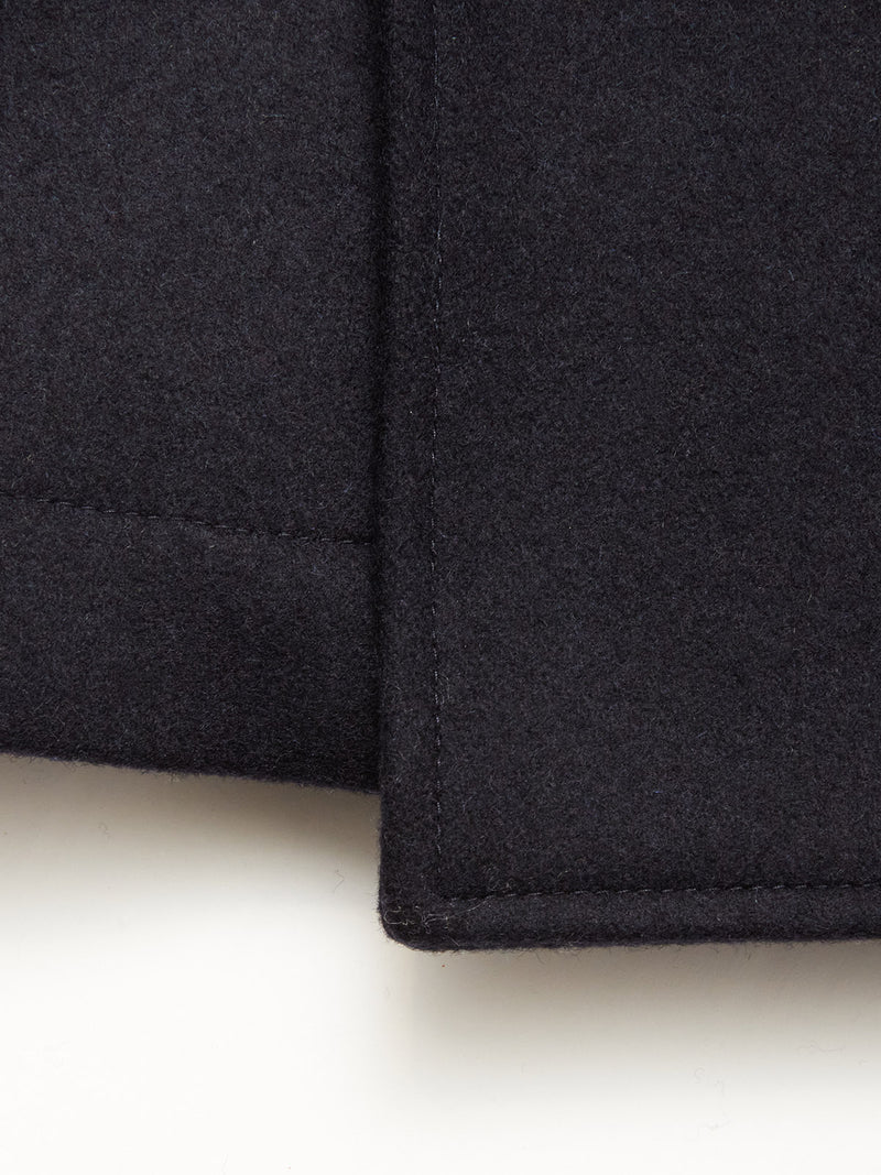 Close-up of the corner of the Blue de Gênes Shiba Melton Coat in Dark Navy, showcasing its thick Italian Melton wool, precise stitching, and sharp edges against a light background.